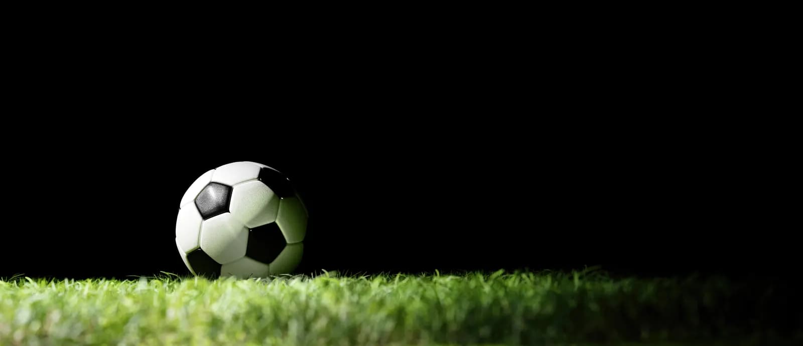Fußball auf grünem Rasen vor schwarzem Hintergrund