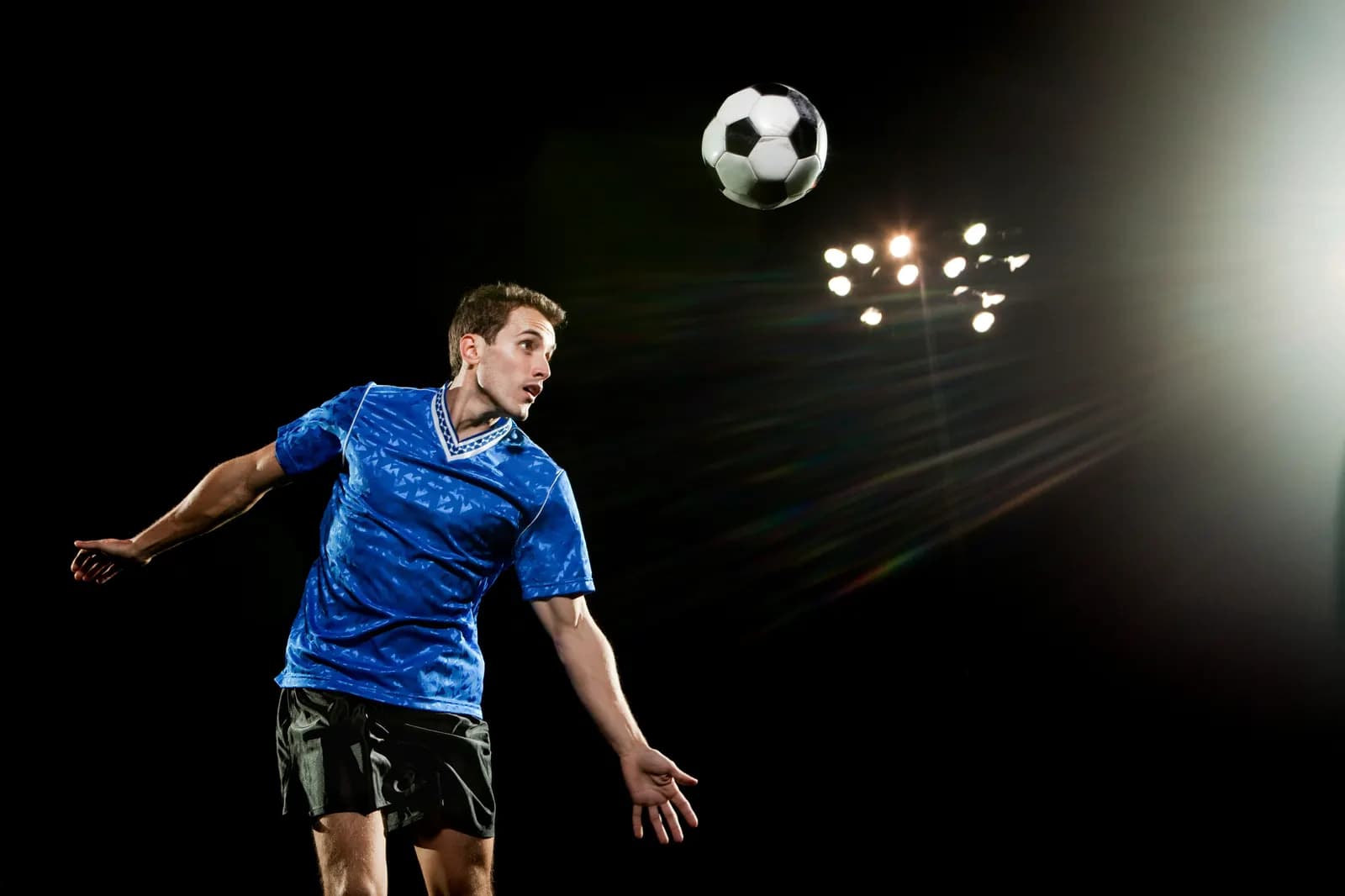 Spieler köpft den Ball unter grellem Flutlicht