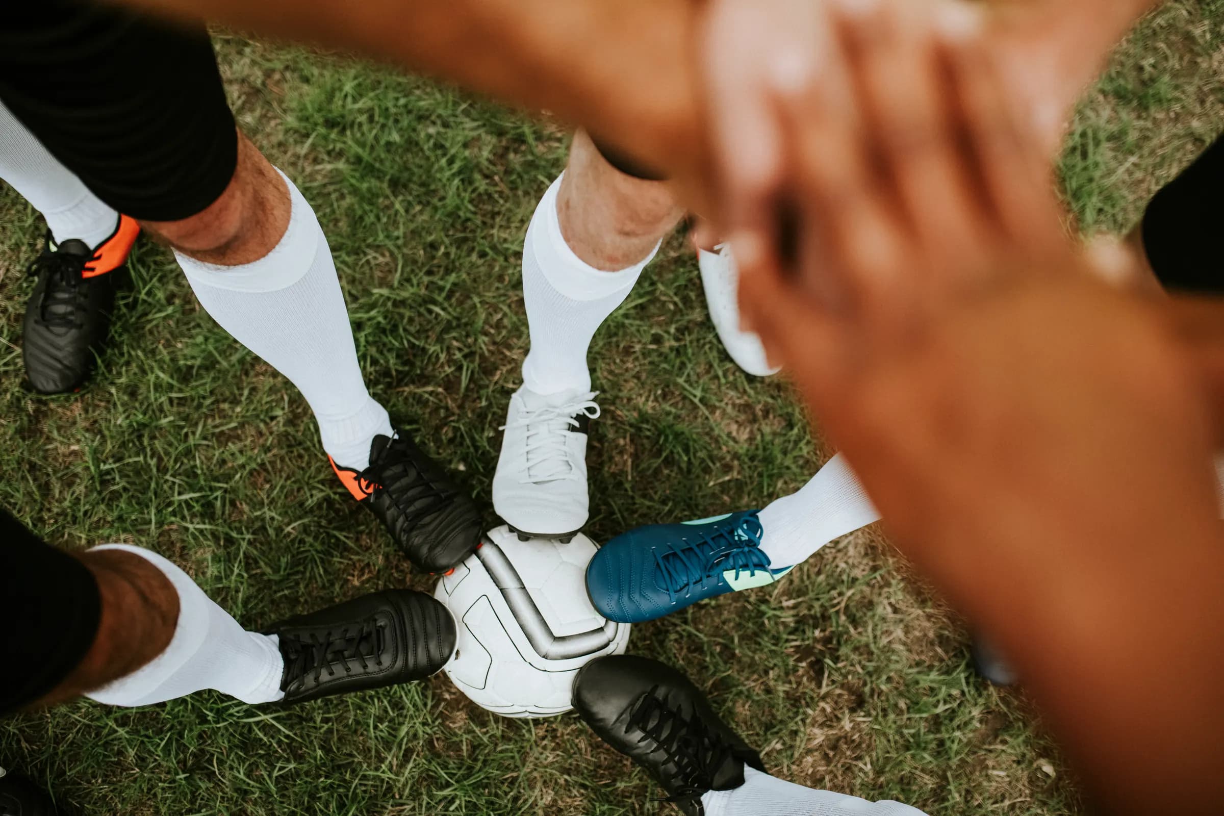 Teamkreis auf dem Rasen, Hände übereinander am Ball